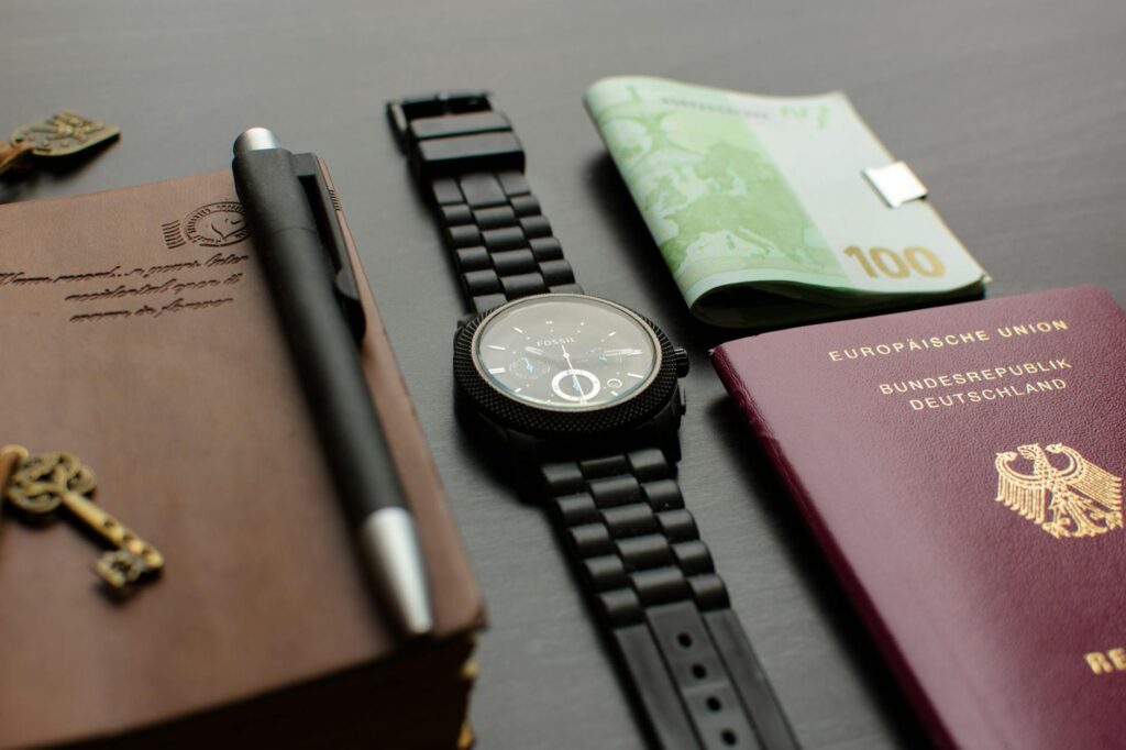 round black chronograph watch on table near germany passport an banknote on table